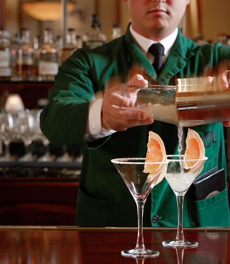 Bartender pouring cocktail into martini glasses with citrus garnish in Denver, CO bar setting