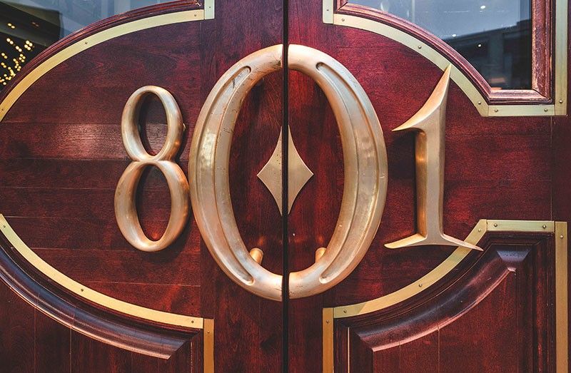 Entrance doors with large 801 emblem at 801 Chop House featuring polished wood and brass details