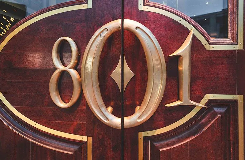 Entrance doors with large 801 emblem at 801 Chop House featuring polished wood and brass details